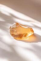 A smooth golden amber piece lies elegantly on a gently toned surface, illuminated by soft, natural light. The warm gradient backdrop creates a serene focus on the amber photo