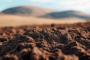Close-up view of freshly plowed dark brown soil illuminated by soft sunlight, highlighting its rich texture. Rolling hills fade into the background, creating an inviting and organic atmosphere photo
