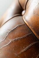 Detailed view of an aged leather sofa highlighting its cracks and faded color. Soft lighting accentuates its texture, perfect for showcasing restoration potential photo