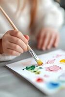 Small hands are actively dipping brushes into vibrant watercolor paints, creating a colorful masterpiece on a table. The softly blurred background enhances the focus on this artistic activity photo