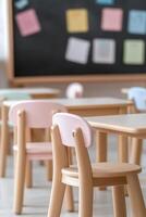 This primary school classroom features small wooden desks arranged neatly, with colorful posters adorning the walls. Soft lighting creates a warm and inviting atmosphere for students photo