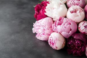 Deep pink and red peonies are arranged beautifully against a dark backdrop. Soft lighting highlights their delicate textures while creating a moody atmosphere perfect for marketing photo