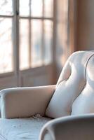 This soft fabric armchair, set in a bright reading nook, displays visible dust, discoloration, and lint, creating a softly blurred yet inviting atmosphere for upholstery cleaning photo