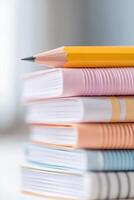 A bright and colorful collection of notebooks is organized on a school desk, finished with a sharpened pencil on top, embodying a productive and studious environment photo
