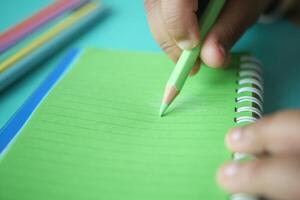 Writing with green pencil on lined notebook in a bright setting photo