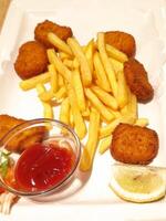 Crispy golden chicken nuggets alongside french fries, garnished with ketchup and lemon wedge on pristine white ceramic plate photo