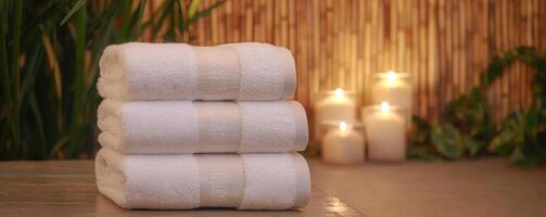 Relaxing spa self-care day concept. Soft white towels stacked with candles and greenery in a serene spa setting. photo
