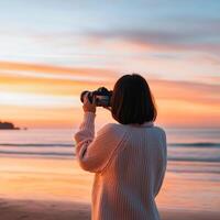 Travel blogger taking pictures concept. Person photographing a sunset at the beach in a cozy sweater. photo