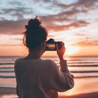 Travel blogger taking pictures concept. A person capturing a sunset on the beach with a camera. photo