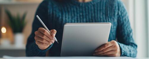 Digital transformation e-learning courses concept. Person writing on a tablet with a pen, dressed in a cozy sweater, in a softly lit environment. photo