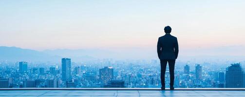 Inspirational success story motivation concept. A man stands overlooking a city skyline at dusk, reflecting on the view before him. photo