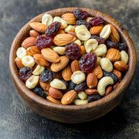 A bowl of mixed nuts and dried fruits on a textured surface. photo
