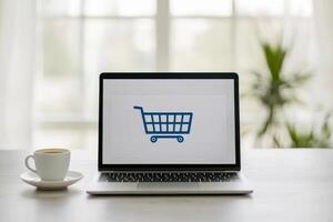 e-commerce checkout process concept Laptop displaying a shopping cart icon beside a coffee cup in a bright, modern setting. photo