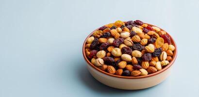 Nut trail mix with dried fruits concept. A bowl of mixed nuts and dried fruits on a light blue background. photo