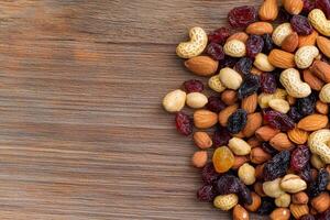 Nut trail mix with dried fruits concept. A variety of nuts and dried fruits scattered on a wooden surface. photo