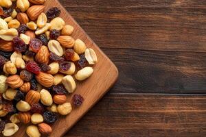 Nut trail mix with dried fruits concept. Assorted nuts and dried fruits on a wooden board background. photo