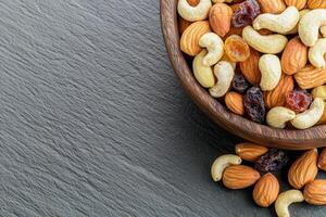 Nut trail mix with dried fruits concept. Mixed nuts and dried fruits in a wooden bowl on a gray surface. photo