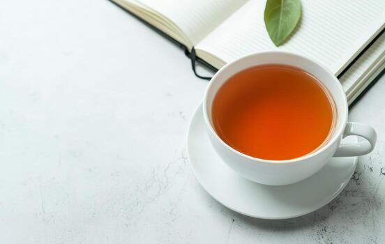 Wellness positivity and productivity concept. A cup of tea beside an open notebook on a textured surface. photo