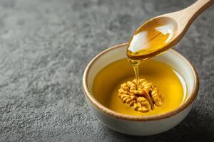 Walnut oil in glass bottle concept. A spoon drizzles oil over a walnut in a small bowl, set against a textured background. photo