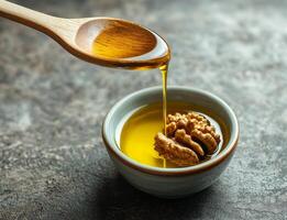 Walnut oil in glass bottle concept. Golden oil being drizzled from a wooden spoon into a small bowl with walnuts. photo