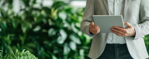 Sustainable business corporate concept. Professional holding a tablet amidst lush greenery in a modern setting. photo