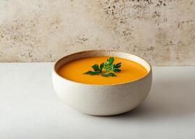 Carrot soup in ceramic bowl concept. Creamy orange soup garnished with herbs in a textured bowl. photo