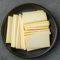 Vegan cheese alternative in dish concept. Sliced cheese on a dark plate against a textured background. photo