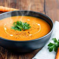 Carrot soup in ceramic bowl concept. Warm carrot soup garnished with herbs in a black bowl. photo