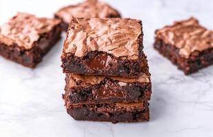 Rich brownie with chocolate chunks concept. Delicious chocolate brownies stacked on a marble surface, showcasing a fudgy interior and a crackly top, perfect for dessert lovers. photo