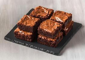 Rich brownie with chocolate chunks concept. Deliciously baked brownies stacked on a slate board, showcasing a rich chocolate texture with a crispy top layer. photo