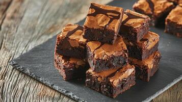 Rich brownie with chocolate chunks concept. Deliciously rich chocolate brownies stacked on a slate serving board, showcasing a glossy, cracked surface and a moist, fudgy interior. photo