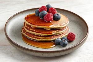 Plant-based diets Food concept. Pancakes topped with fresh blueberries and raspberries, drizzled with syrup, served on a rustic plate. photo