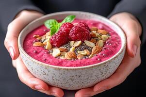 Plant-based diets Food concept. Smoothie bowl topped with raspberries, nuts, and seeds, held in hands, showcasing a healthy and delicious meal. photo
