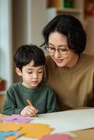 Personalized learning for education concept. A mother and son engage in a creative activity, focusing on colorful paper shapes at a table, showcasing a nurturing and educational moment. photo