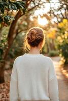 Self-care routines for Wellness concept. A woman in a white sweater stands with her back to the camera, surrounded by trees and sunlight, enjoying a tranquil outdoor moment. photo