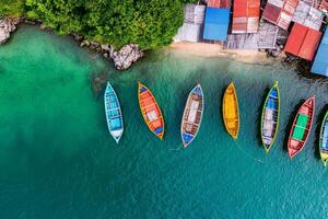 Adventure and Eco-tourism for travel concept. Colorful boats lined up on clear turquoise waters, surrounded by lush greenery and rustic cabins along the shore. photo