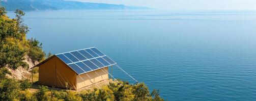 Adventure and Eco-tourism for travel concept. Tent with solar panels overlooks a calm sea, surrounded by lush greenery and mountains in the distance. photo