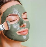 Self-care routines for Wellness concept. Woman applies a green facial mask, showcasing a skincare routine, with serene expression and soft lighting. photo