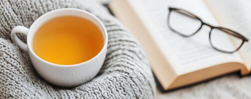 Self-care and healthy aging for wellness. Cup of tea, a book, and glasses on a knitted blanket, perfect for relaxation and reading. photo