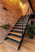 Home improvement with sustainable building concept. Staircase with wooden steps and a stylish black railing against a backdrop of exposed brick walls and greenery. photo