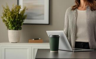 Business entrepreneurship with remote work concept. Workspace featuring a woman beside a laptop, a green coffee cup, and a decorative plant, creating a cozy and productive atmosphere. photo