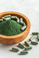 Health supplements and natural remedies concept. Bowl of green powder and capsules on a textured surface. photo