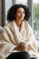 Lifestyle wellness with mental health and self-care concept. Cozy woman wrapped in a blanket enjoying a warm drink by the window. photo