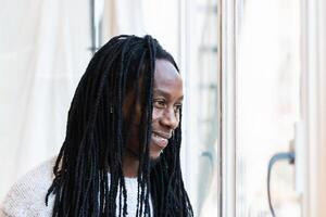 A man with dreadlocks standing in front of a window photo