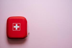 This is a Compact Red First Aid Kit featuring a distinctive White Cross prominently displayed against a Pink Background, designed for easy accessibility in emergencies photo