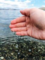 A persons hand is carefully reaching out toward a beautiful body of water, hoping to touch its smooth surface or perhaps feel a gentle wave lapping against their fingers photo