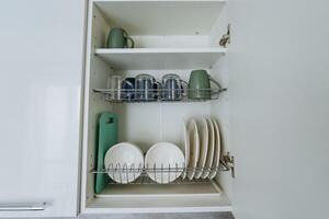 In a wellorganized kitchen, a cabinet is entirely packed with a variety of items, including plates, cups, and even a cutting board, which serves both food preparation and serving needs photo