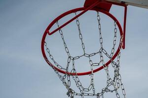 This is a closeup view of a basketball hoop, featuring chains, set against the backdrop of a clear blue sky. It highlights the essence of athletic activity and recreation photo