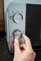 A person is actively pressing a button on a microwave oven, which is a highly popular kitchen appliance renowned for its ability to quickly heat and cook a variety of foods with efficiency photo