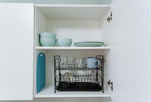 In a wellorganized kitchen cabinet, youll find various essential items such as plates, bowls, cups, glasses, and a cutting board neatly arranged for easy access and storage photo